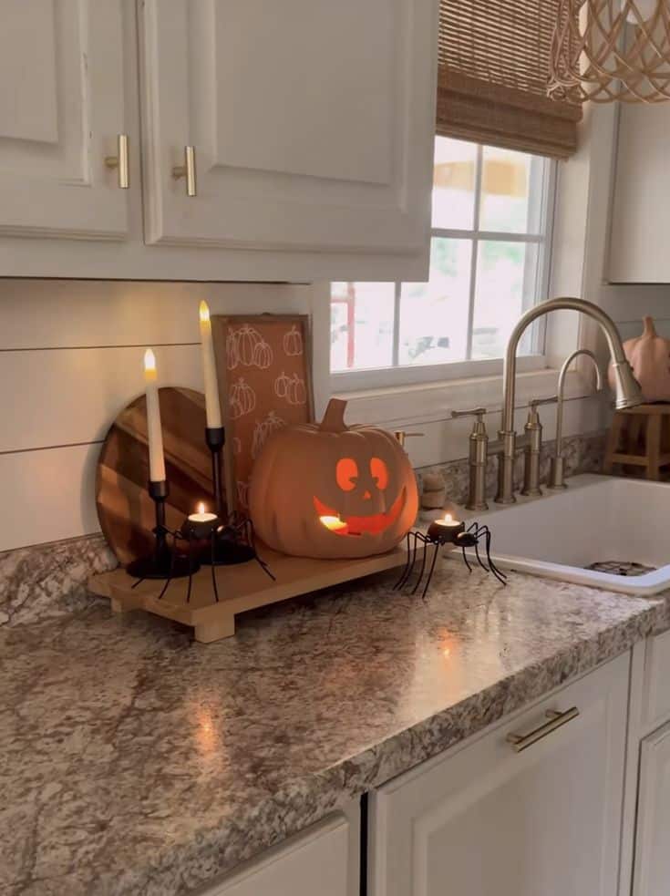 Cozy Halloween kitchen decor with a glowing jack-o'-lantern, candles, and spider accents on a granite countertop.