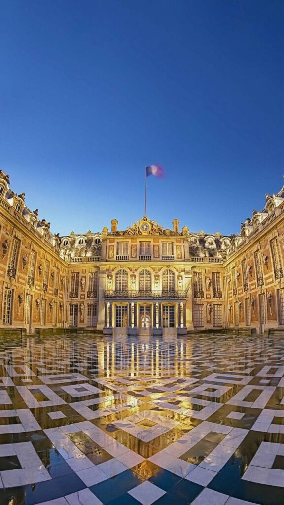 Exterior view of the Palace of Versailles courtyard with French flag and intricate tiled floor under clear blue sky.