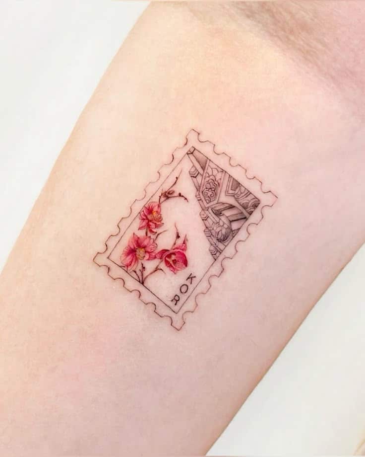 Delicate skin tattoo of a postage stamp with pink flowers and intricate design elements.