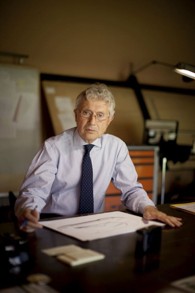 Architect at desk reviewing blueprints in an office setting with drawing tools.