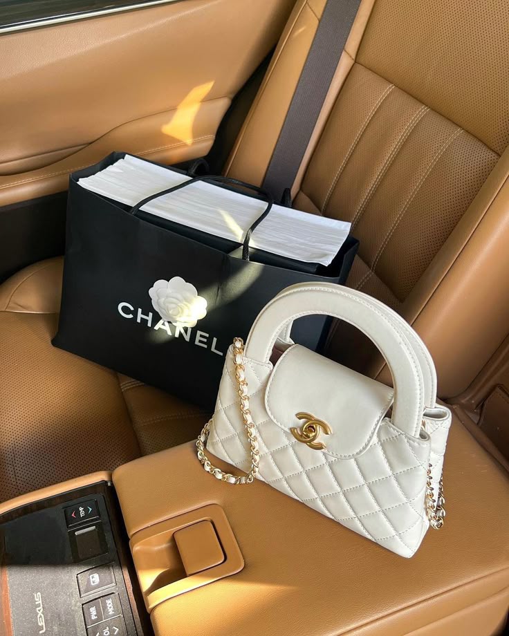 67a78643-de55-4ad4-8062-2b4de2b724e2 White Chanel handbag with chain on car seat beside branded shopping bag. Luxurious style and elegant design. | Sky Rye Design White Chanel handbag with chain on car seat beside branded shopping bag. Luxurious style and elegant design.