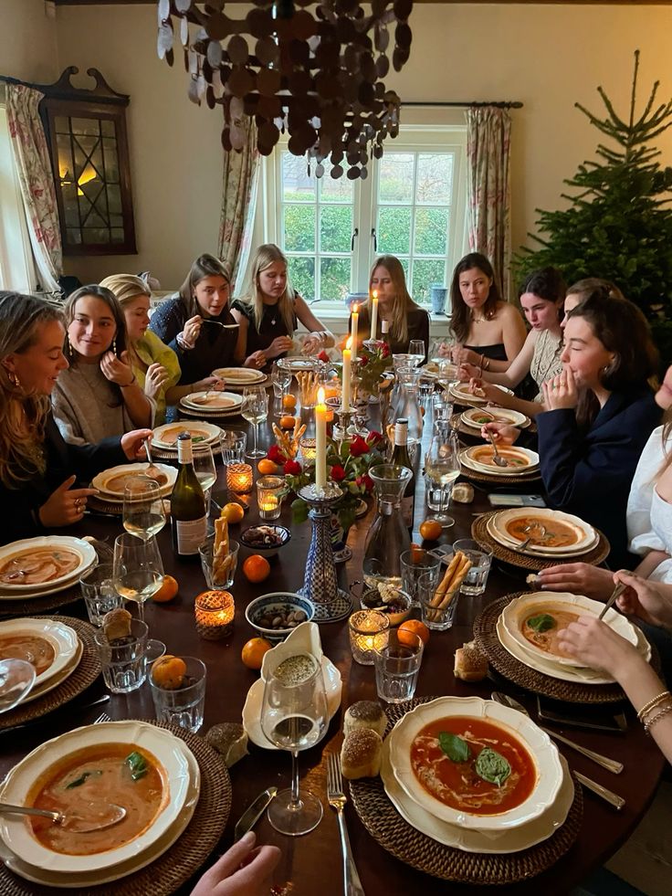 Festive dinner gathering with friends enjoying candlelit meal around a large table, warm atmosphere, and holiday decor.