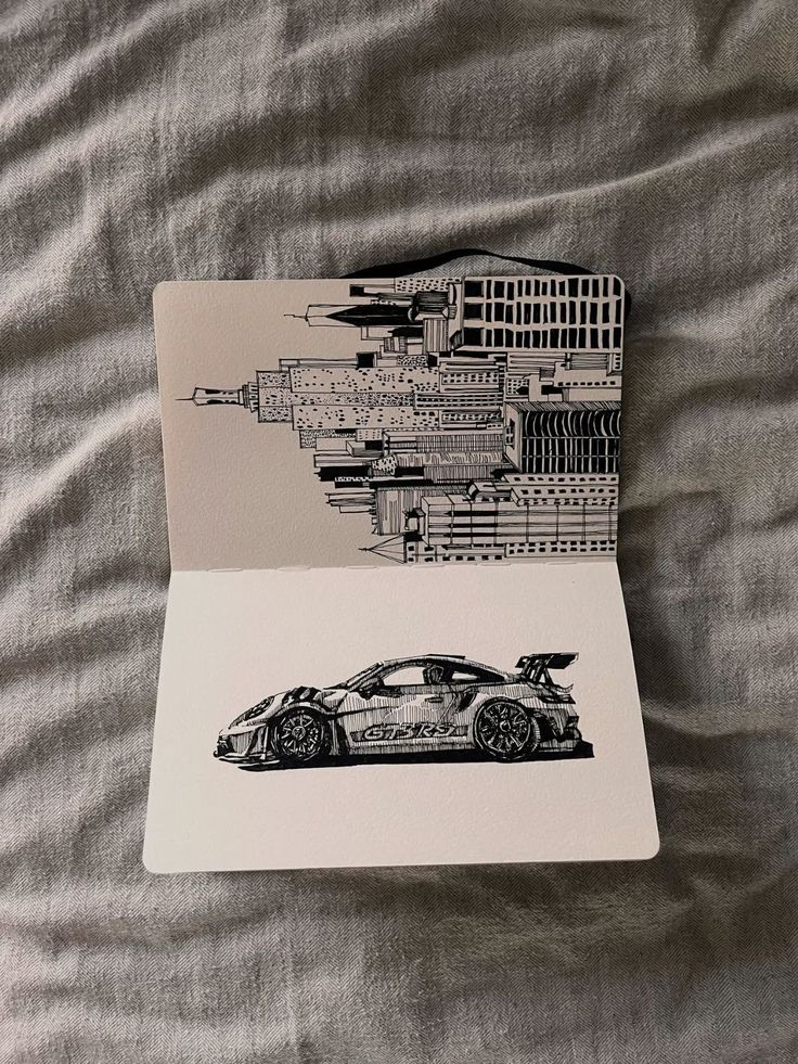 6b060cab-4060-497f-9921-12c123189a82 Open sketchbook with illustrations of a city skyline and a racing car on textured fabric background. | Sky Rye Design Open sketchbook with illustrations of a city skyline and a racing car on textured fabric background.