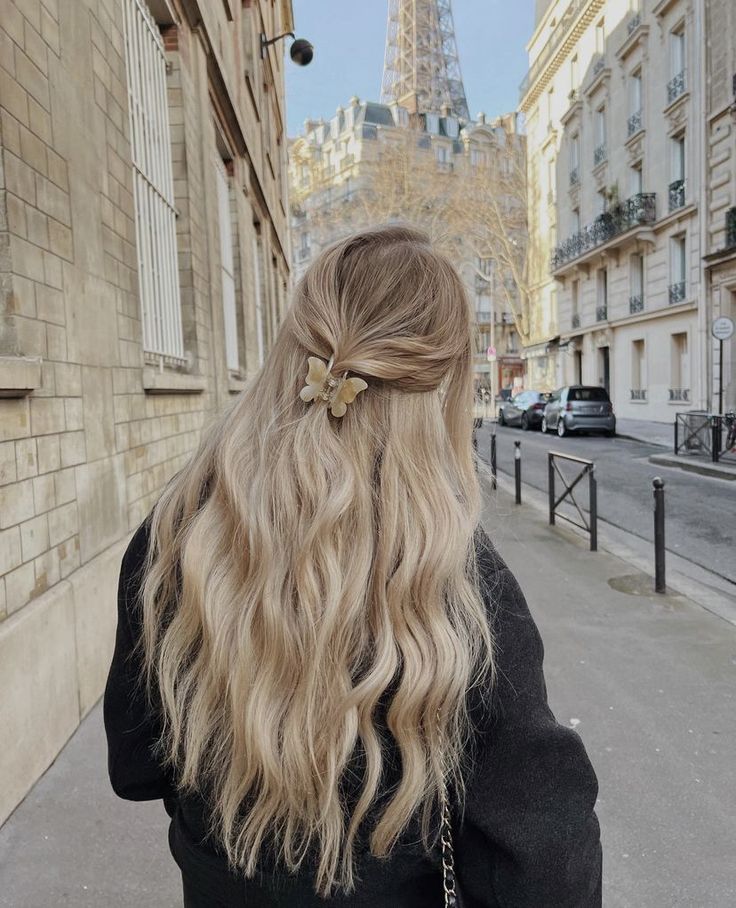 Person with wavy blonde hair and clip facing Eiffel Tower on Parisian street.