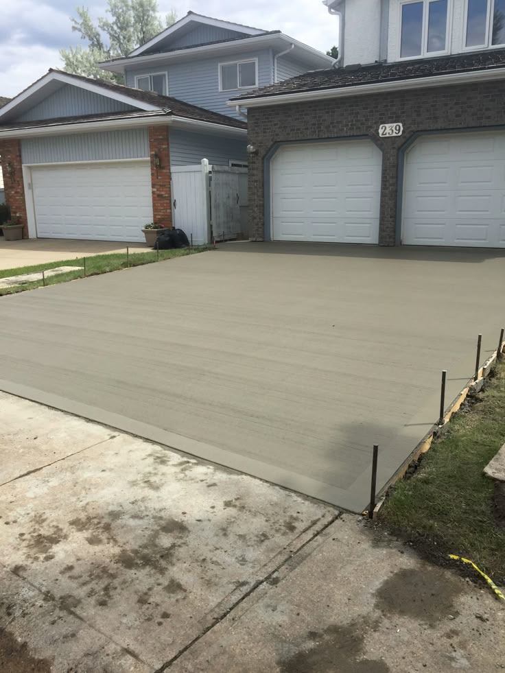 Freshly laid concrete driveway in front of a residential garage, with framing stakes still in place.