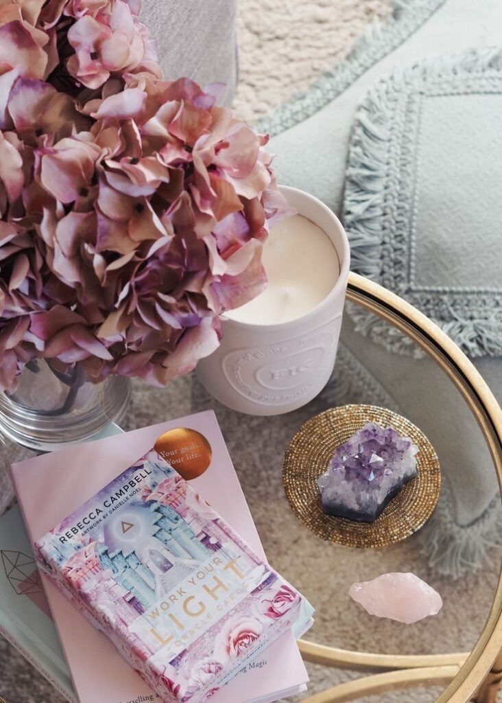 Cozy setting with pink hydrangeas, a white candle, crystals, and books on a glass table.