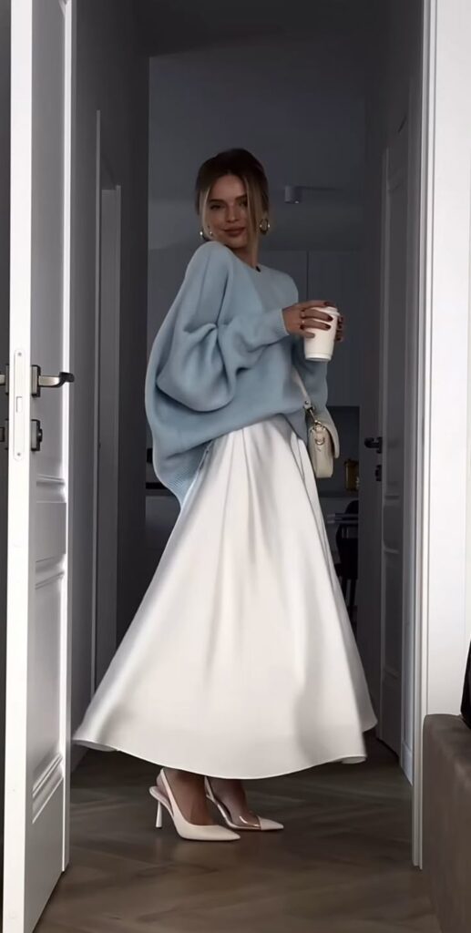 _ 7 Woman in blue sweater and white skirt holding coffee, standing in a doorway, fashionably dressed in heels and earrings. | Sky Rye Design Woman in blue sweater and white skirt holding coffee, standing in a doorway, fashionably dressed in heels and earrings.