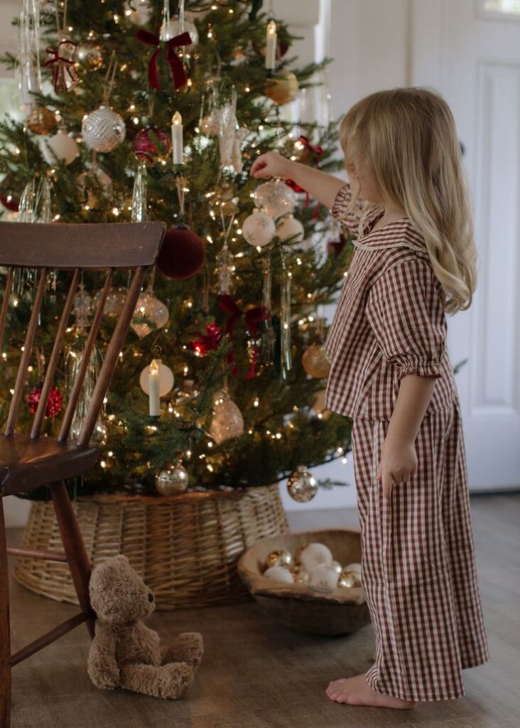 Child decorating a Christmas tree with ornaments and lights, cozy holiday scene indoors.
