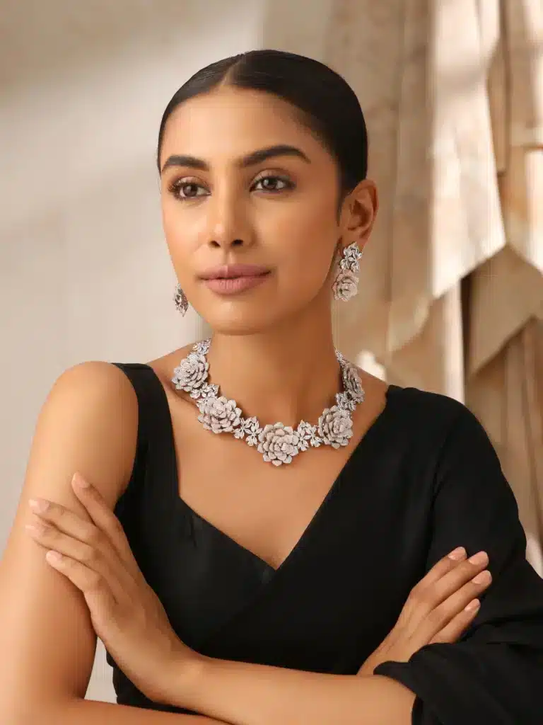 Elegant woman in black dress wearing floral diamond necklace and matching earrings, posing confidently indoors.
