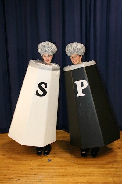 Two people dressed in salt and pepper shaker costumes with shower cap lids against a blue curtain backdrop.