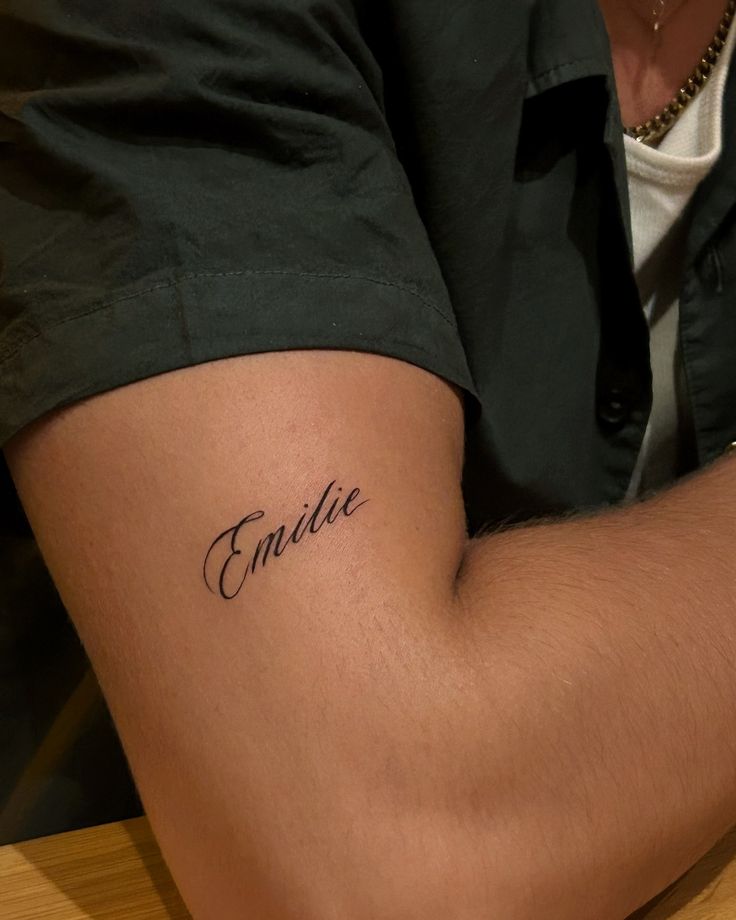 Arm tattoo with the name “Emilie” in elegant script font, showcased on a relaxed bicep.
