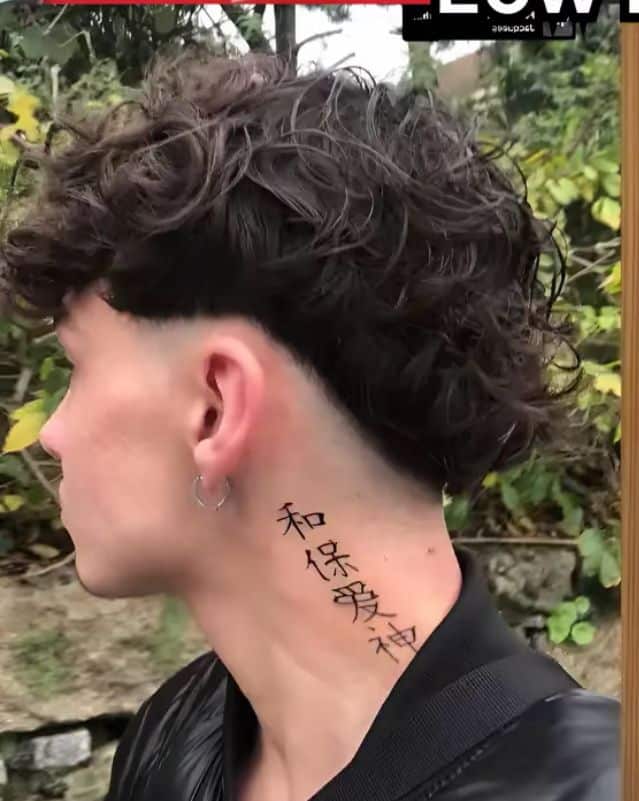 Person with curly hair and neck tattoo featuring Chinese characters, wearing a black jacket outdoors.