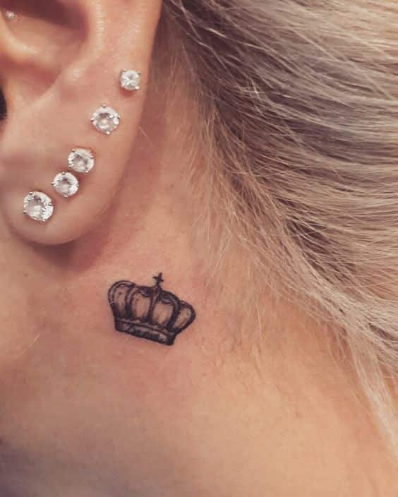 _ 8 Crown tattoo behind ear with multiple diamond piercings on ear, highlighting a stylish and elegant look. | Sky Rye Design Crown tattoo behind ear with multiple diamond piercings on ear, highlighting a stylish and elegant look.