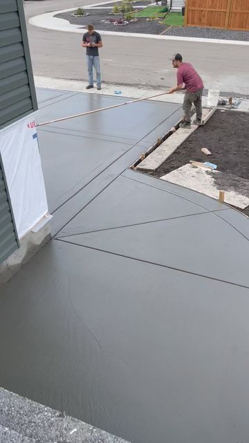 Two construction workers finishing a freshly poured concrete driveway in a residential area.
