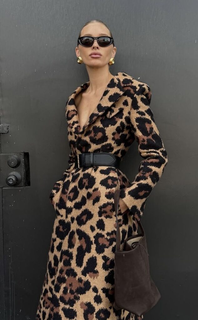 Screenshot Fashionable woman in leopard print coat, black sunglasses, and gold earrings, poses confidently with a brown handbag. | Sky Rye Design Fashionable woman in leopard print coat, black sunglasses, and gold earrings, poses confidently with a brown handbag.