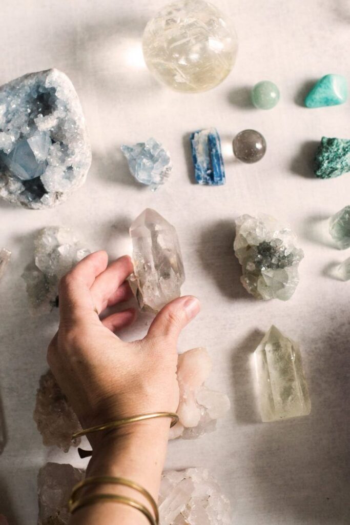 Hand selecting various healing crystals and gemstones on a light surface.