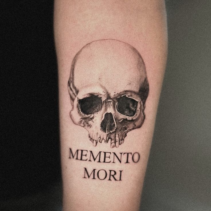 Skull tattoo with text Memento Mori on arm, emphasizing mortality and reflection.