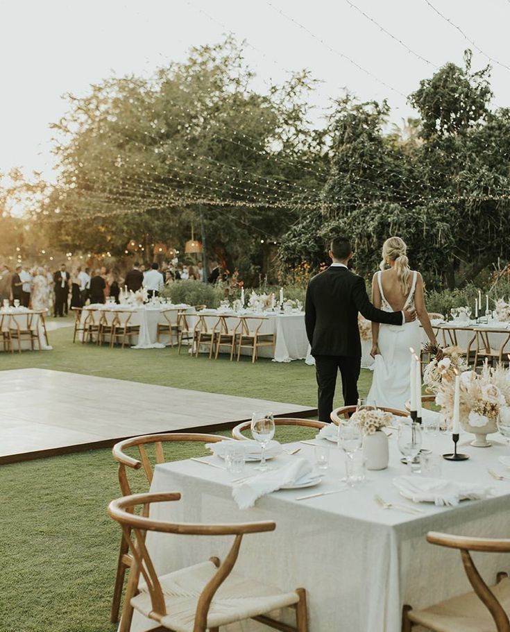 Elegant outdoor garden wedding reception with decorated tables, bride and groom walking, and string lights overhead. wedding