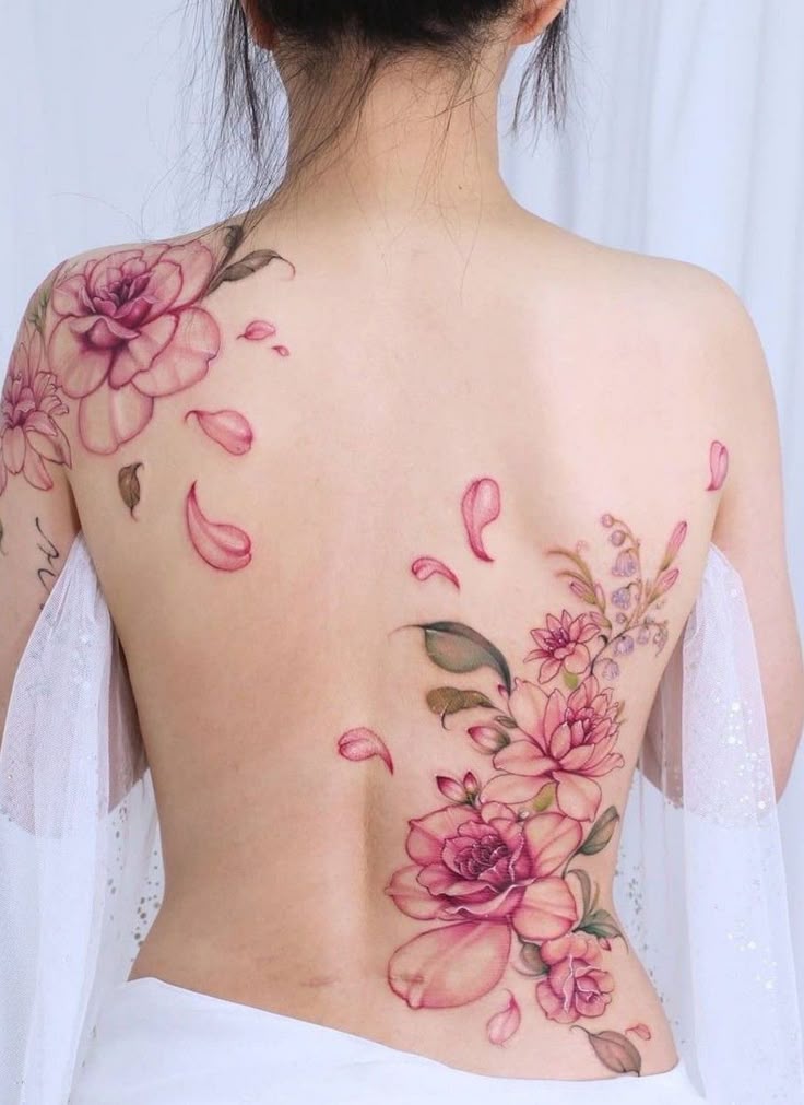 809826a6-e167-4625-9538-d0a4863c20d8 Back tattoo of pink florals and petals on a woman wearing a white wrap, showcasing delicate and intricate design. | Sky Rye Design Back tattoo of pink florals and petals on a woman wearing a white wrap, showcasing delicate and intricate design.