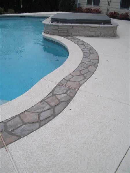 Curved stone path design beside a modern swimming pool and spa with light concrete deck.