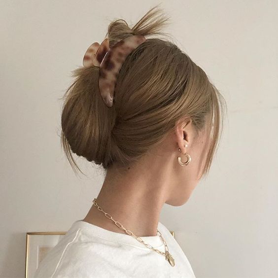 Woman with updo hairstyle and tortoiseshell hair clip, wearing gold jewelry and white top, side profile.