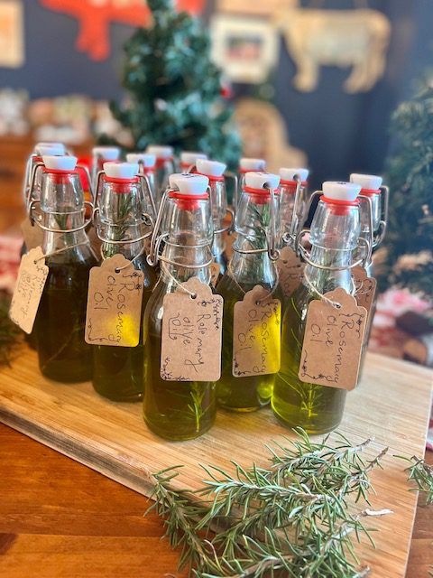 Bottles of handmade rosemary oil with tags, arranged on a wooden board, surrounded by fresh rosemary sprigs.