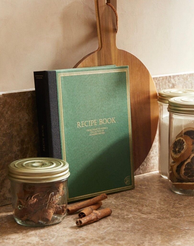 8d0458ebbc7c7e8b15b349bc96ab2aa8 Green recipe book with wooden cutting board and spice jars on a kitchen counter. | Sky Rye Design Green recipe book with wooden cutting board and spice jars on a kitchen counter.