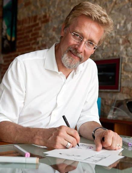 Smiling man with glasses drawing on paper in a studio setting.
