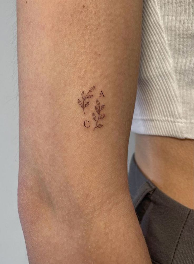 _ 9 Minimalist leaf and letter tattoo on forearm, featuring small delicate plant designs with initials A and C. | Sky Rye Design Minimalist leaf and letter tattoo on forearm, featuring small delicate plant designs with initials A and C.