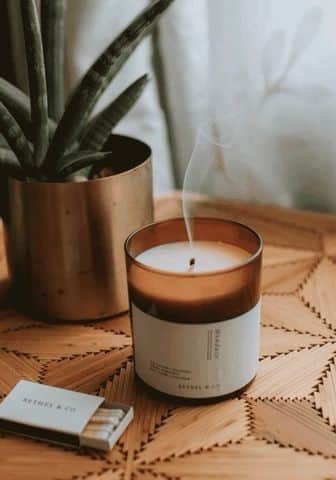 _ 9 Scented candle with smoke on a wooden table near a plant, creating a cozy and serene ambiance. | Sky Rye Design Scented candle with smoke on a wooden table near a plant, creating a cozy and serene ambiance.