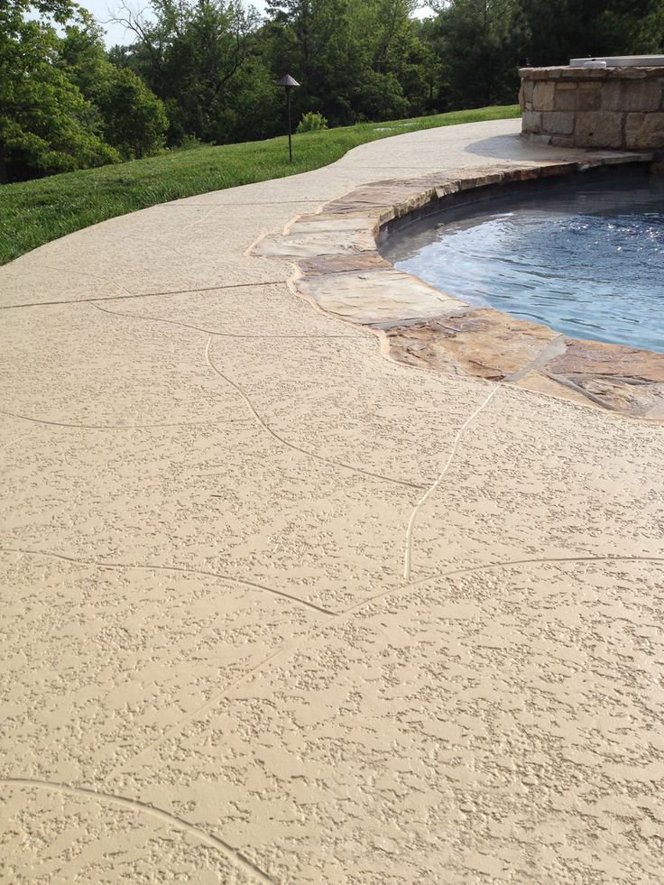 Textured concrete patio with a rock-edge pool, surrounded by greenery. Ideal for outdoor relaxation and design inspiration.