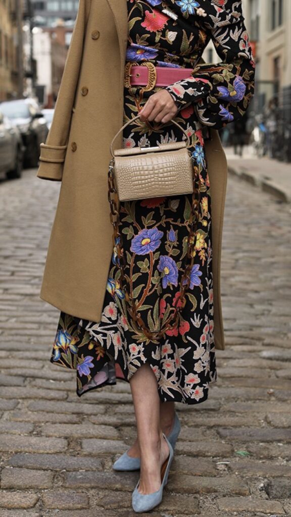 _ 9 Stylish woman in floral dress, camel coat, and blue heels holding a textured handbag on cobblestone street. Fashionable look. | Sky Rye Design Stylish woman in floral dress, camel coat, and blue heels holding a textured handbag on cobblestone street. Fashionable look.