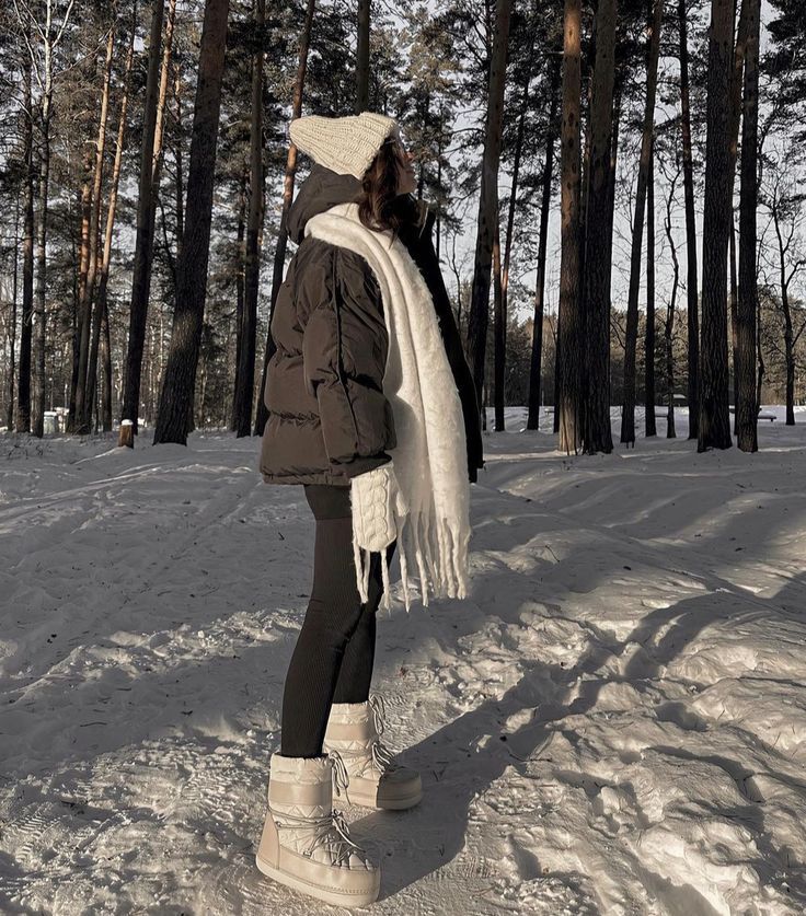 Woman in winter clothing enjoys a snowy forest walk, wearing a cozy jacket, scarf, and boots under the tall trees.