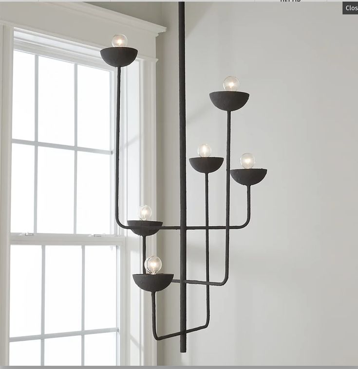 Modern black chandelier with multiple bulbs hanging by a window in a minimalist room.