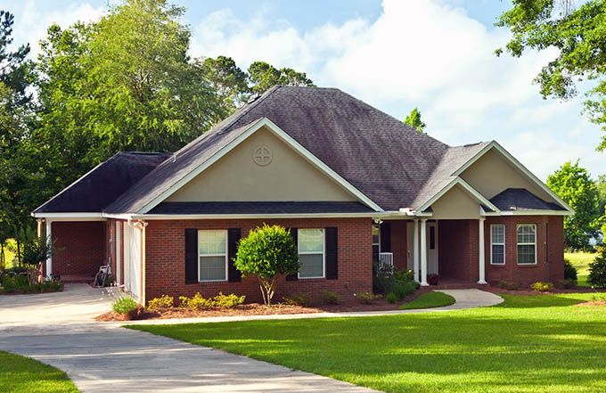 Brick suburban house with manicured lawn and driveway under a sunny sky.