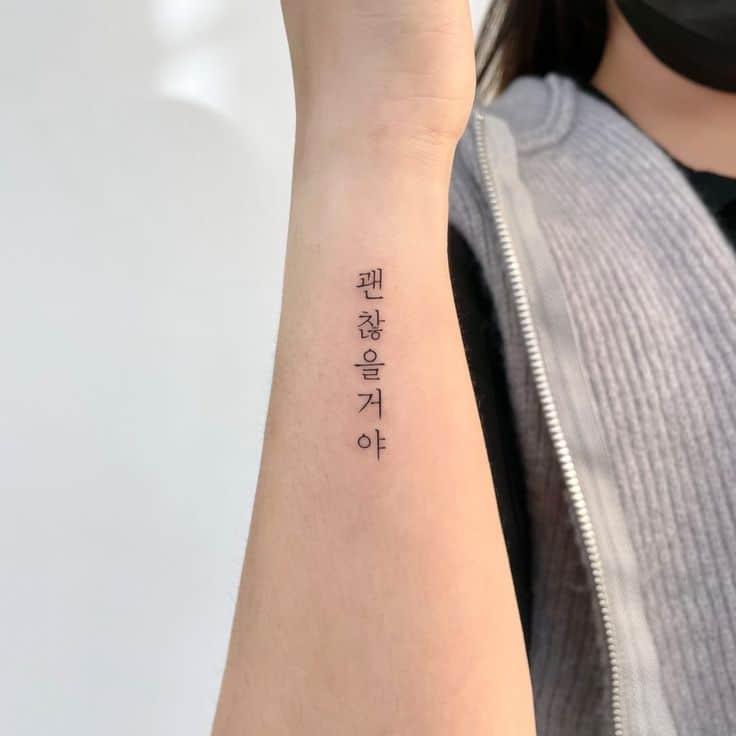 Arm with Korean script tattoo in black ink, person wearing a gray vest and face mask.