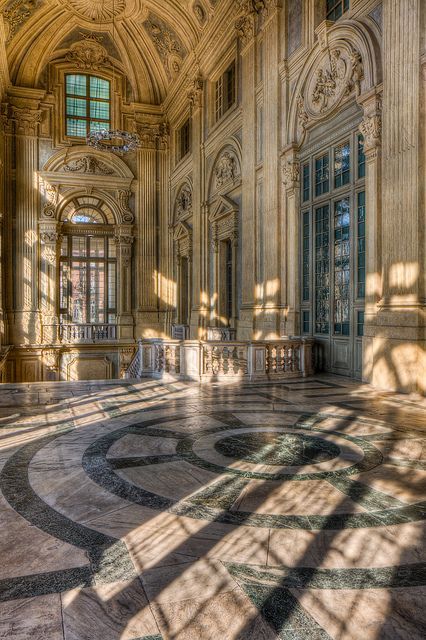 Elegant sunlit interior of an ornate historical building with marble flooring and intricate architectural details.
