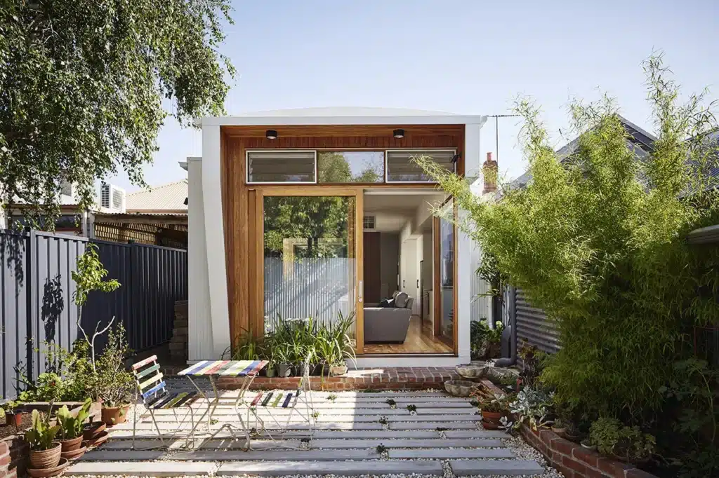 94265_1280px Modern tiny house with wooden accents, patio, and lush garden greenery in a suburban backyard setting. | Sky Rye Design Modern tiny house with wooden accents, patio, and lush garden greenery in a suburban backyard setting.