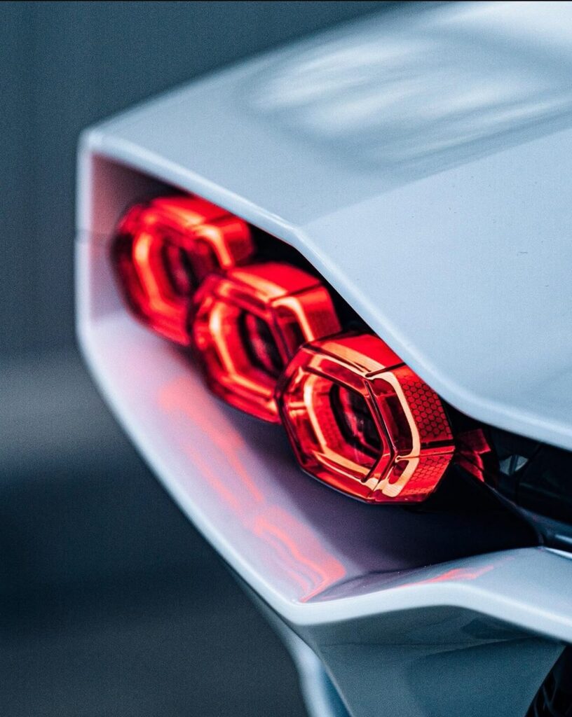 9505ed32ae236e32e5c264e30f7af171 Close-up of sleek red hexagonal tail lights on a modern sports car, showcasing its futuristic design. | Sky Rye Design Close-up of sleek red hexagonal tail lights on a modern sports car, showcasing its futuristic design.