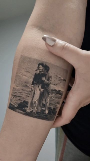 Tattoo of a couple on a beach, depicted on a person's arm, with a close-up view of the detail and texture.