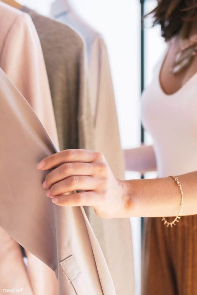 9619f7e2-2d41-45de-b841-e7ea206f8131 Woman browsing clothes on a rack, selecting a beige coat. Fashion shopping concept. | Sky Rye Design Woman browsing clothes on a rack, selecting a beige coat. Fashion shopping concept.