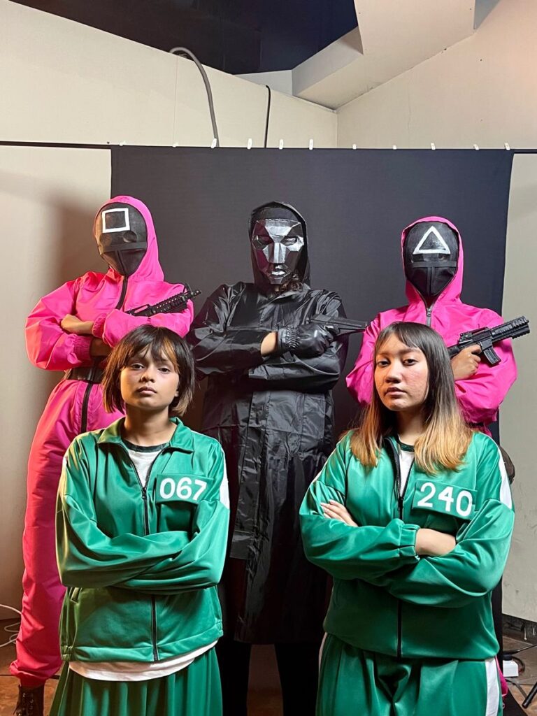 Group in colorful costumes with masks, likely from a popular TV show, posing together indoors.