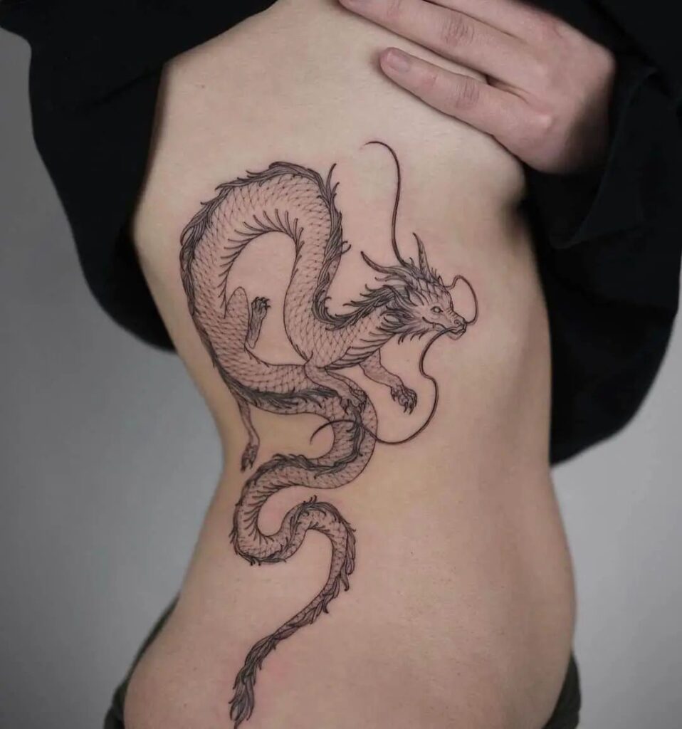 Intricate dragon tattoo on ribs, showcasing detailed scales and flowing design. Black ink art on skin.