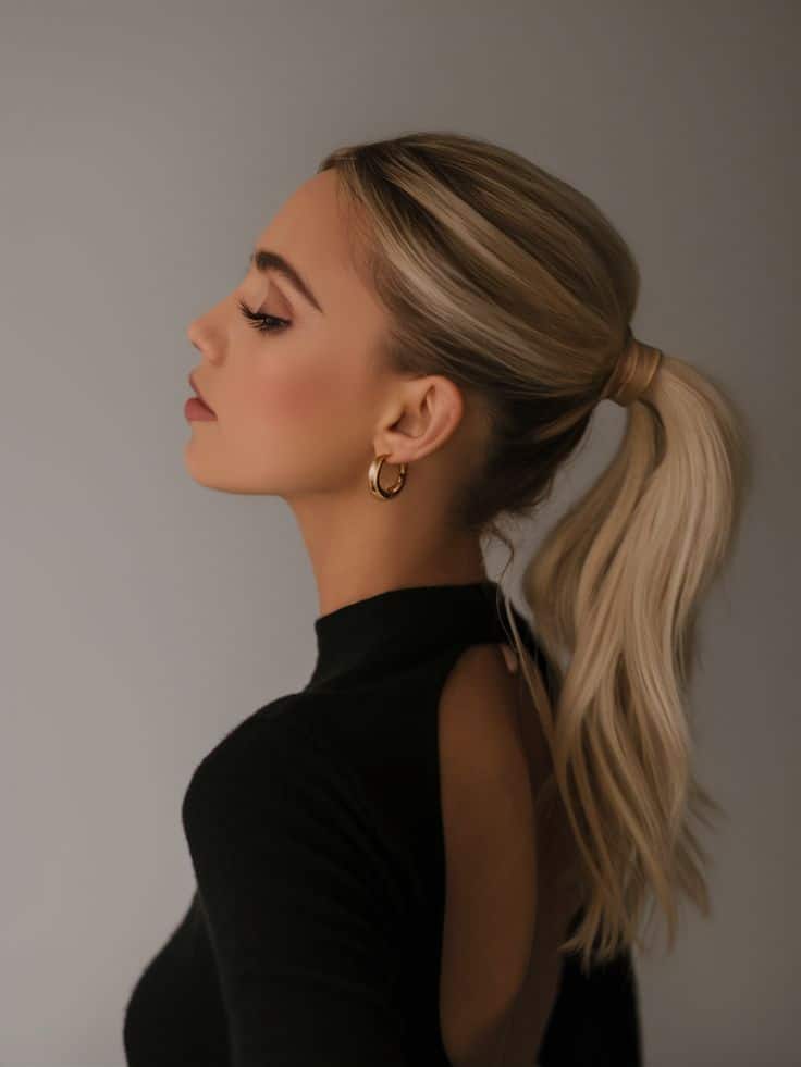 Profile of a woman with blonde ponytail and gold hoop earrings wearing a black open-back top. Elegant and fashionable.