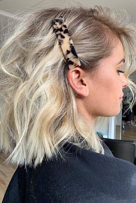 Blonde woman with wavy bob hairstyle and tortoiseshell hair clip, side profile view in a salon setting.