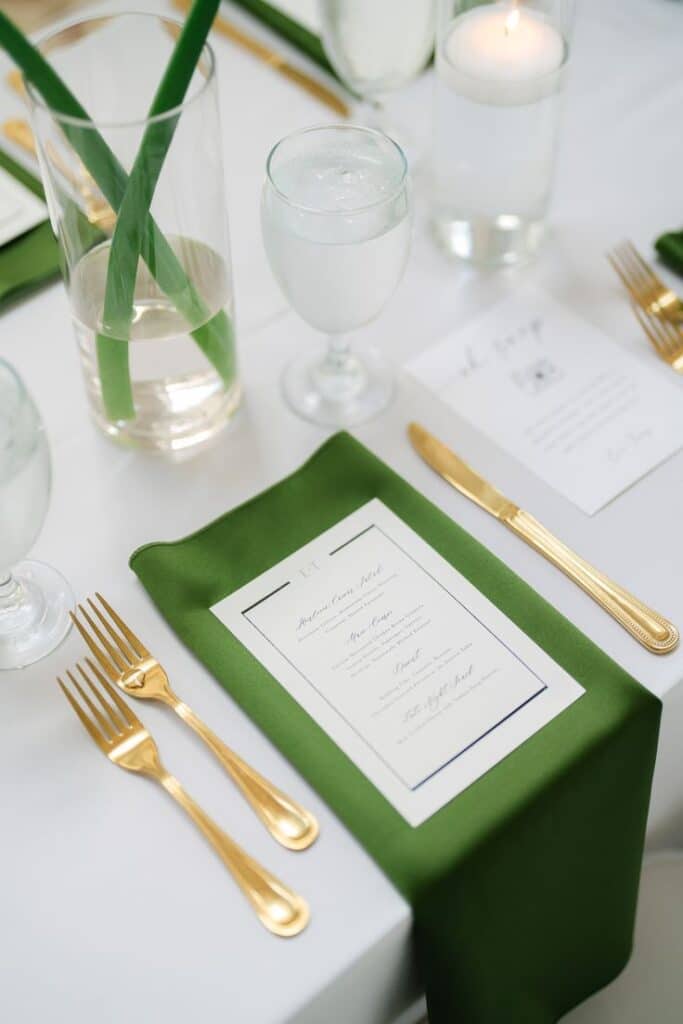 Elegant table setting with green napkin, gold cutlery, menu, and glassware, ideal for weddings or formal events.