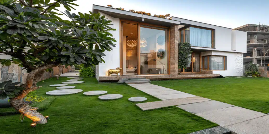 A sustainable home along a landscape Modern house with large windows, lush garden, circular stepping stones, and sleek exterior design. | Sky Rye Design Modern house with large windows, lush garden, circular stepping stones, and sleek exterior design.