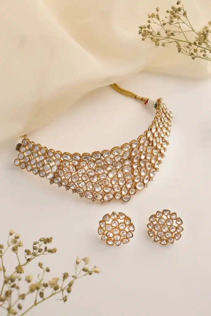 Elegant gold necklace and earrings set with crystal detailing, displayed on a white background with delicate flowers.