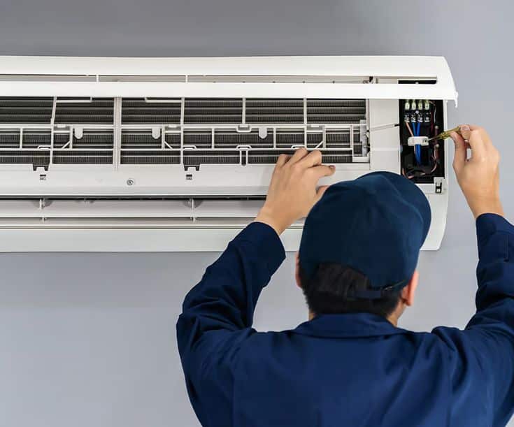 Technician repairing wall-mounted air conditioner unit, focusing on wiring and maintenance.