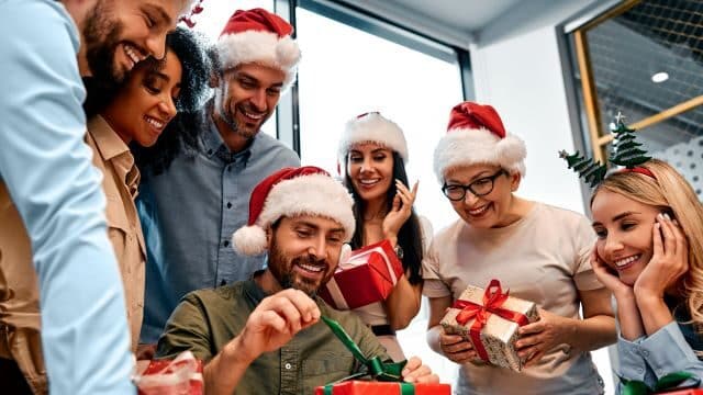 Group of people in Santa hats exchanging gifts at a festive holiday celebration, smiling and enjoying the moment.